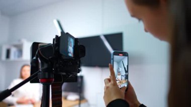 Bir kadın blogcunun videosunu aynı anda iki cihaza yüklemek. Tripoddaki profesyonel kamera bir konuşmayı kaydediyor ve kadın akıllı telefonuyla video çekiyor. Günlük konsepti.