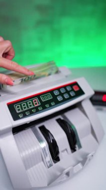 Kadın eli, para sayma makinesine 100 avroluk yığınla banknot koyuyor. Banka ekipmanları nakit sayar. Kapatın. Dikey video.