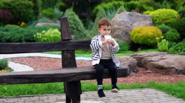 Çekici şirin çocuk güzel bir parkta bankta oturuyor. Bebek abur cubur yiyor..