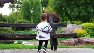 Çizgili tişörtlü beyaz bir çocuk bir bankın üstüne koşuyor. Çocuk bir an için durur ve kaçar..