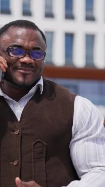 Sportif Afrikalı adam telefonda konuşuyor. Gözlüklü siyahi işadamının portresi şehir dışındaki telefon görüşmesiyle iş dünyasına öncülük ediyor. Dikey video