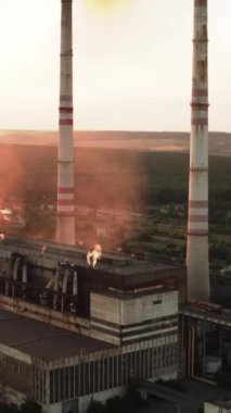 Gün batımında dumanla tehlikeli bir imalat. Endüstriyel fabrika akşamları havayı kirletir. Büyük fabrika bacaları. Atmosferi kirletiyor. Hava görüntüsü. Dikey video