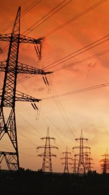 Gün batımında elektrik dağıtım istasyonu. Parlak gökyüzü zemininde kabloları olan yüksek çelik elektrik kuleleri. Yüksek voltajlı elektrik hatları. Yükseliyor. Dikey video