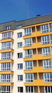 Şehirdeki yeni çok katlı bina. Gökyüzü arka planında şehir sakinleri için yeni bir evin ön cephesinin geniş pencereleri ve renkli duvarları olan çağdaş apartman dairesi. Dikey video