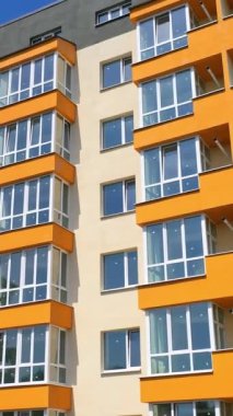 Camlı balkonları olan modern bir bina. Renkli duvarları olan yeni yapılmış apartman bloklarının önü. Şehirdeki yeni apartman cephesi. Dikey video