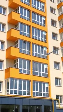 Yeni apartman. Şehirdeki çok katlı bir modern tasarım evinin dışında. Geniş pencereli parlak şehir binası cephesi. Dikey video