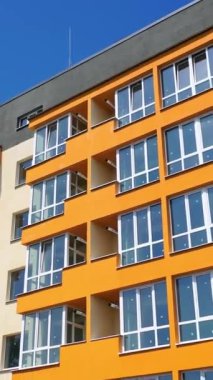 Çok güzel bir bina. Yazın mavi arka planda geniş balkonları olan modern apartman blokları. Renkli duvarlardan oluşan bir apartman. Kamera aşağı iniyor. Dikey video