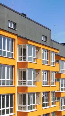 Şehirde yeni bir çok katlı bina. Turuncu duvarlı, geniş balkonlu bir apartmanın modern tasarımı. Şehir sakinleri için lüks bir ev. Dikey video