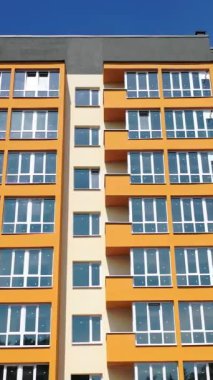 Yeni bir apartmanın ön cephesi. Parlak duvarları olan modern çok katlı bir ev. Geniş balkonlu apartmanlar. Ön manzara. Dikey video
