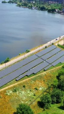 Kırsal bölgedeki enerji güneş enerjisi çiftliği. Photovoltaik güneş pilleri açık yaz gününde nehir kenarında. Alternatif temiz enerji kaynağı. Hava görüntüsü. Dikey video