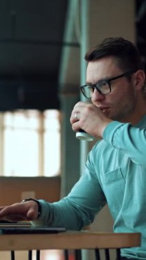 Dizüstü bilgisayarda çalışan ve kağıt bardaktan kahve içen bir adam. Bilgisayarda rahat bir ofiste oturan gülümseyen bir iş adamı. Dikey video