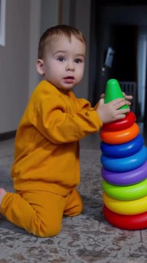 Sevimli bir çocuk elinde oyuncak bir piramitle dizlerinin üstünde duruyor. Turuncu takım elbiseli çocuk oyuncağı düşürür ve kameraya doğru sürünerek yaklaşır. Dikey video