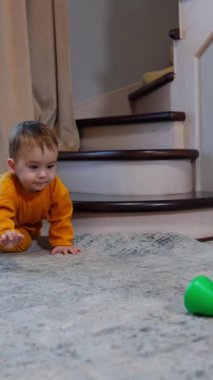 Çocuk oyuncak piramidine tırmanıyor ve tepesine çıkıyor. Bebek dizlerinin üstüne çöküp merakla yukarı bakıyor. Dikey video