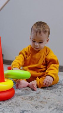 Odada oturan oyuncak piramitle oynayan tatlı çocuk. Sevimli çocuk kamerayı fark ediyor ve neşeyle ona doğru sürünüyor. Dikey video