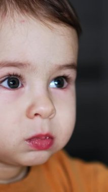 Beslenme sırasında bir yaşında, beyaz bir çocuğun yüzü vardı. Çocuk dikkatlice yana bakıyor ve sonra elini ağzına alıyor. Kapatın. Dikey video
