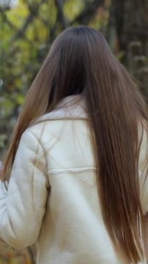 Çekici esmer, sonbahar doğası gereği elinde telefonla yürüyor. Kameradan uzaklaşan bir kadın, bir an için gülümseyip geri dönüyor. Dikey video