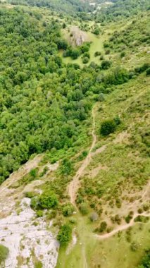 Yürüyüşçülerin patikası dağın yamacında. İnsansız hava aracı kayalık arazide turist yoluna yaklaşıyor. Dikey video.