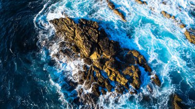 Sudan sarkan çıplak kaya. Beyaz köpüklü dalgalar kayanın yanında. Kıyıdaki güzel okyanus. Üst görünüm.