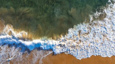 Turuncu kumlu sahilde köpüklü beyaz dalgalarla okyanusun berrak turkuaz suyu. Okyanus kıyısı ya da kıyı şeridi. Üst görünüm.
