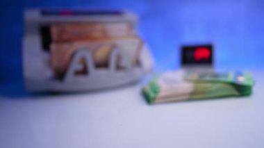 Para sayma makinesi turuncu euro faturalarını sayıyor. Yanında bir yığın yeşil banknot var. Bulanık görüntü. Kapat..
