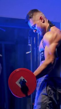Genç, vahşi seksi, güçlü vücut geliştirme sporcusu, halter pompalayan spor adamı. Karın kasları vücut geliştirme konsepti. Mavi ışık filtresi. Dikey video