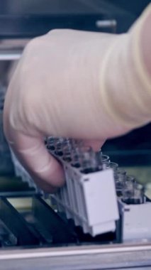 Laboratuvardaki çağdaş ekipmanlar. Laboratuvar çalışanının elleri klinikteki modern makineye şişeler koyuyor. Kan örneklerini test etmek için modern bir alet. Dikey video