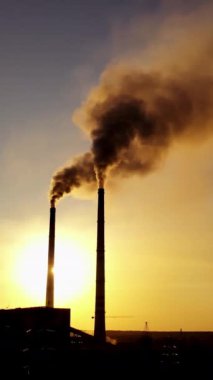 Gün batımında karanlık bir fabrikanın silueti. Akşamları kirli metalürjik bitki dumanı olan borular. Dikey video