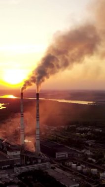 Doğa arasındaki sanayi bitkisi. Gün batımında fabrika borularının insansız hava aracı görüntüleri. Metalürjik bitki ve duman bacalardan geliyor. Dikey video