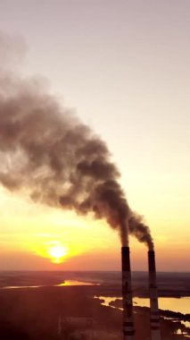Endüstriyel arazi. Gün batımında santralin borularından duman çıkıyor. Çevre kirliliği. Dikey video