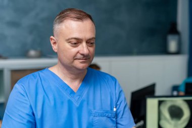 Doktor hasta dosyalarını kontrol ediyor. Mavi önlüklü tıp uzmanı, bir klinikte yapılacak konsültasyona hazırlanırken hasta verilerini gözlemler..