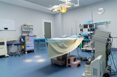 Modern hastane cerrahi odası. Parlak ve temiz cerrahi odasında tıbbi ekipmanlar, bir ameliyat masası ve bir prosedür için personel hazırlıkları yer almaktadır..