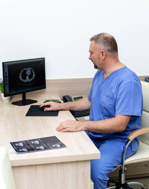 Doktor ofiste görüntüleri inceliyor. Bir tıp uzmanı, sağlık merkezinde otururken akciğer taramalarını bilgisayarda inceler..
