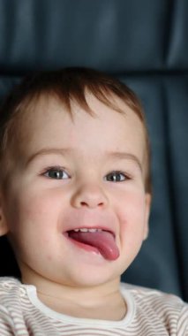 Komik, şakacı erkek bebek ofis sandalyesinde oturuyor. Sevimli çocuk kameraya dil gösteriyor. Kapatın. Dikey video