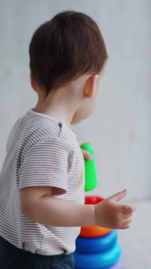 Bir yaşındaki çocuk bir piramitle oynuyor. Oyuncağı parçalara ayıran ve sonra tekrar toplayan bir çocuğun arka görüntüsü. Dikey video