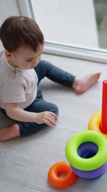 Güzel beyaz çocuk üsse renkli yüzükler takıyor. Küçük çocuk oyuncak piramidiyle oynuyor. Üst Manzara. Dikey video
