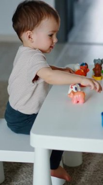 Sevimli bebek masada oyuncaklarla oynuyor. Çocuk bardağı itiyor ve yuvarlanışını izliyor. Dikey video