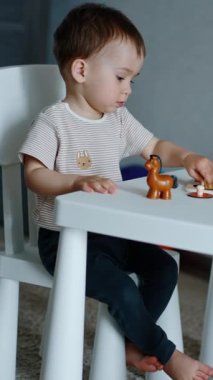 Tatlı küçük çocuk masada oturan oyuncaklarla oynuyor. Hayvanlar üzerinde çalışan sevimli bir çocuk. Dikey video
