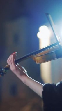 Siyah ceketli yaratıcı bir kız şehirde bir gece fenerinden gelen ışığın arka planında romantik bir melodi çalıyor. Dikey videoyu kapat