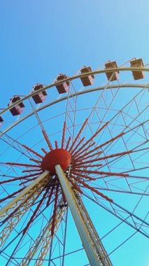 Mavi gökyüzünde dönme dolap. Mavi gökyüzü ve güneşli bir gün lunaparkta dikey video