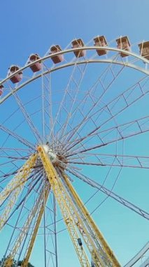 Renkli gondollu dönme dolap. Mavi gökyüzü ve güneşli bir gün lunaparkta dikey video