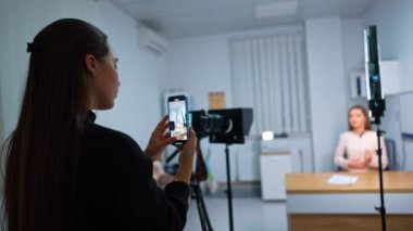 Genç bir kadın elinde telefonuyla dikilip video kaydediyor. İnternet günlüğü için içerik kaydediliyor. Bulanık arkaplan.