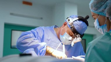 Cerrahi lensler takan cerrahlar ameliyata odaklanmış durumda. Meşgul doktor onları iki elinde tutan aletler kullanıyor..