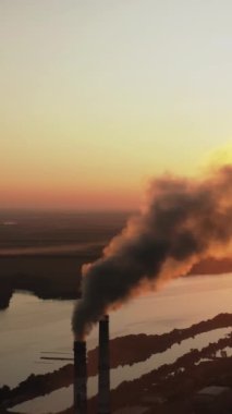 Gün batımında endüstriyel bacalardan kirli duman. Akşamları atmosfere karanlık kimyasal dumanlar salıyor. Çevrede zararlı emisyonlar. Hava görüntüsü. Dikey video