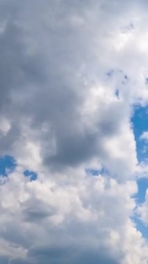 Yumuşak beyaz bulutlar hızla gökyüzünde süzülüyor. Yumuşak bulutlar büyük bir bulutun içinde toplanıyor. Düşük açılı zaman dilimi. Dikey video