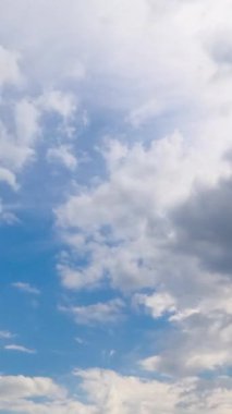 Hafif bulutlu mavi yaz gökyüzü. Parlak güneşin aydınlattığı yumuşak beyaz bulutlar. Zaman ayarlı. Dikey video