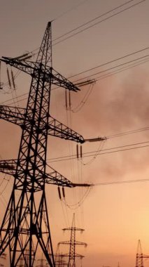 Gün batımında elektrik direkleri duman yığınlarına karşı. Akşam gökyüzünde yüksek voltajlı elektrik kuleleri. Dumanlı fabrika boruları havayı kirletiyor. Hareket kamerası devre dışı. Dikey video