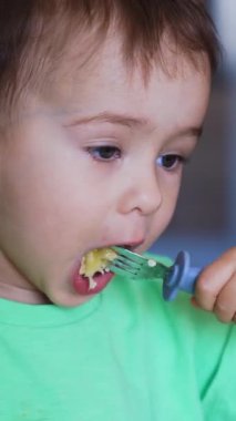 Güzel beyaz bebek çataldan iyi besleniyor. Sandalyede yemek yiyen tatlı bir bebek. Kapatın. Dikey video