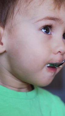 Koyu renk saçlı güzel çocuk kaşıkla besleniyor. Küçük çocuğun beslenmesi. Kapatın. Arkaplan bulanık. Dikey video