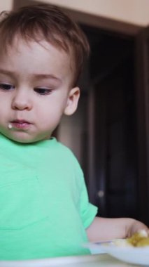 Güzel erkek bebek formdan yemek yemek için çalışıyor. Anne çocuğunu kaşıkla besliyor. Düşük açı. Dikey video