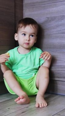 Meraklı çocuk elinde yiyecek bir şeyler tutarak yerde oturuyor. Sevimli bebek ayağa kalkar ve kameraya yaklaşır. Düşük açı. Dikey video
